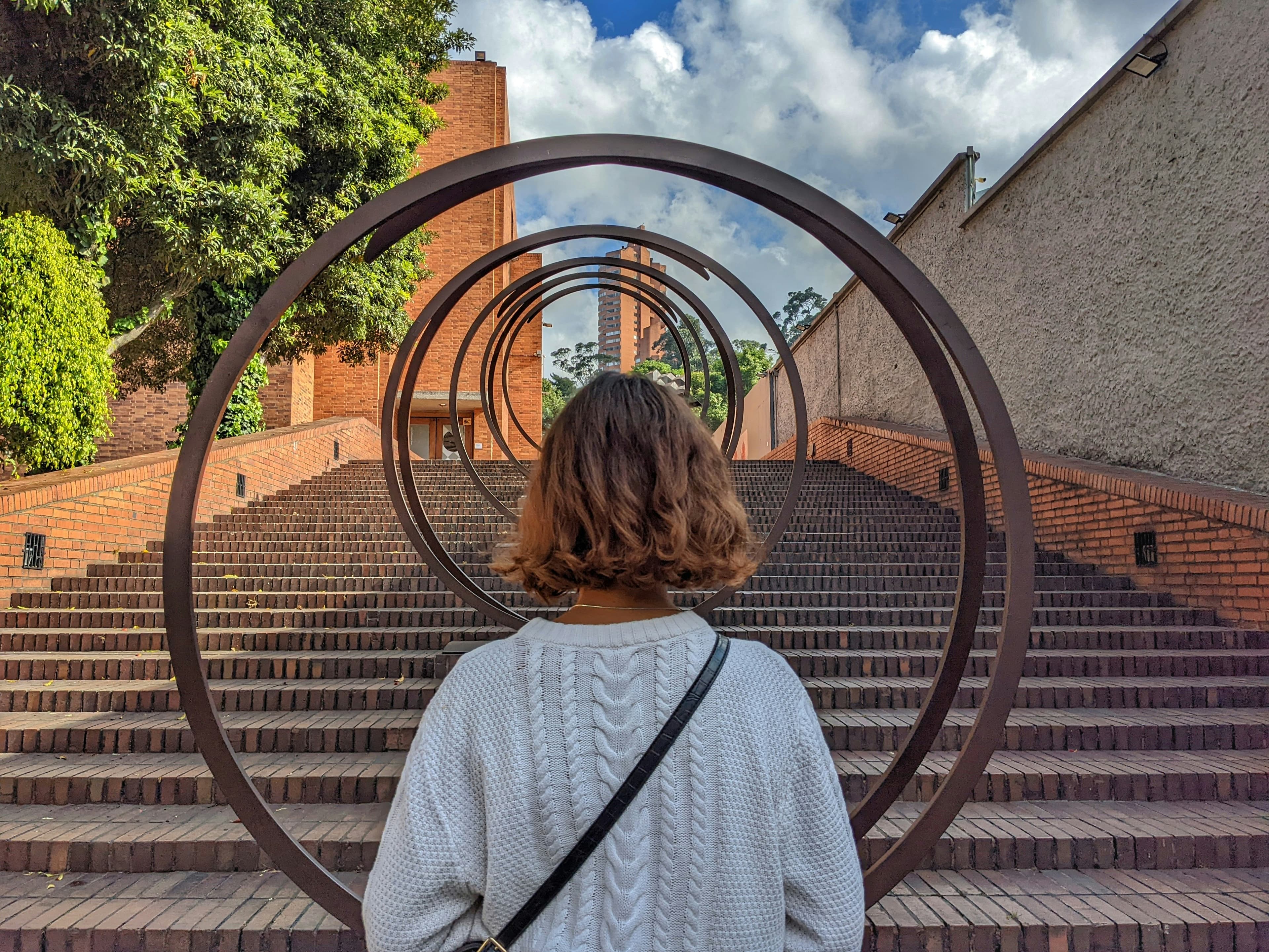 Caminante frente a una escultura de aros en una escalinata de la ciudad